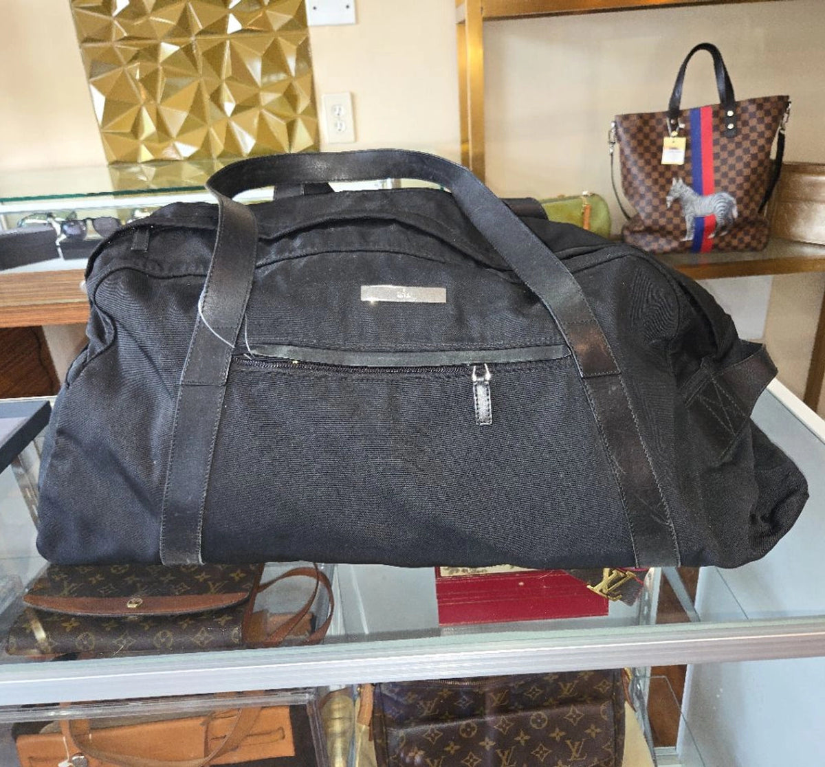 A large black canvas duffel bag with dark brown leather handles and trim